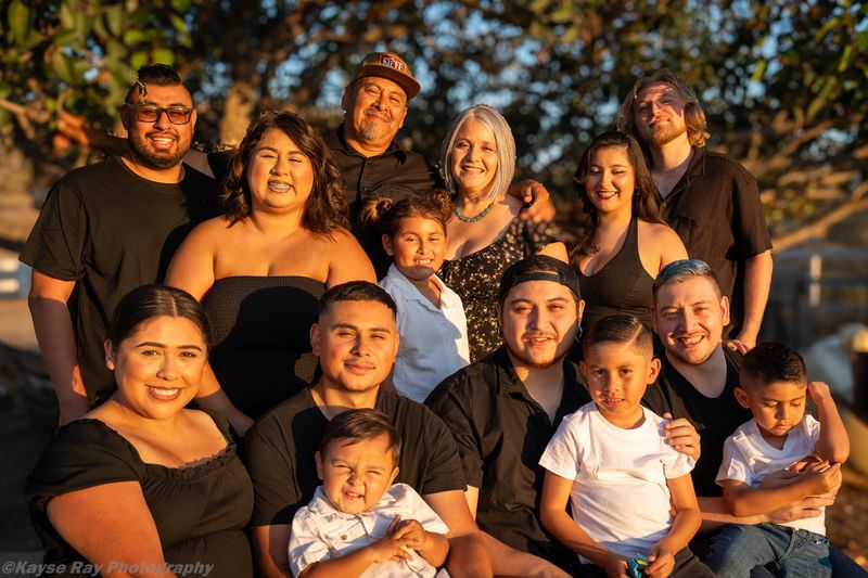A large three-generation family of thirteen poses together bathed in golden sunset light.