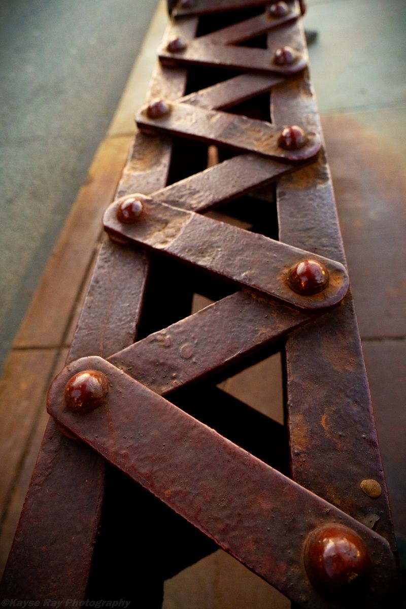 Rusted iron lattice of a scissor-style railing zigzagging away in warm evening light